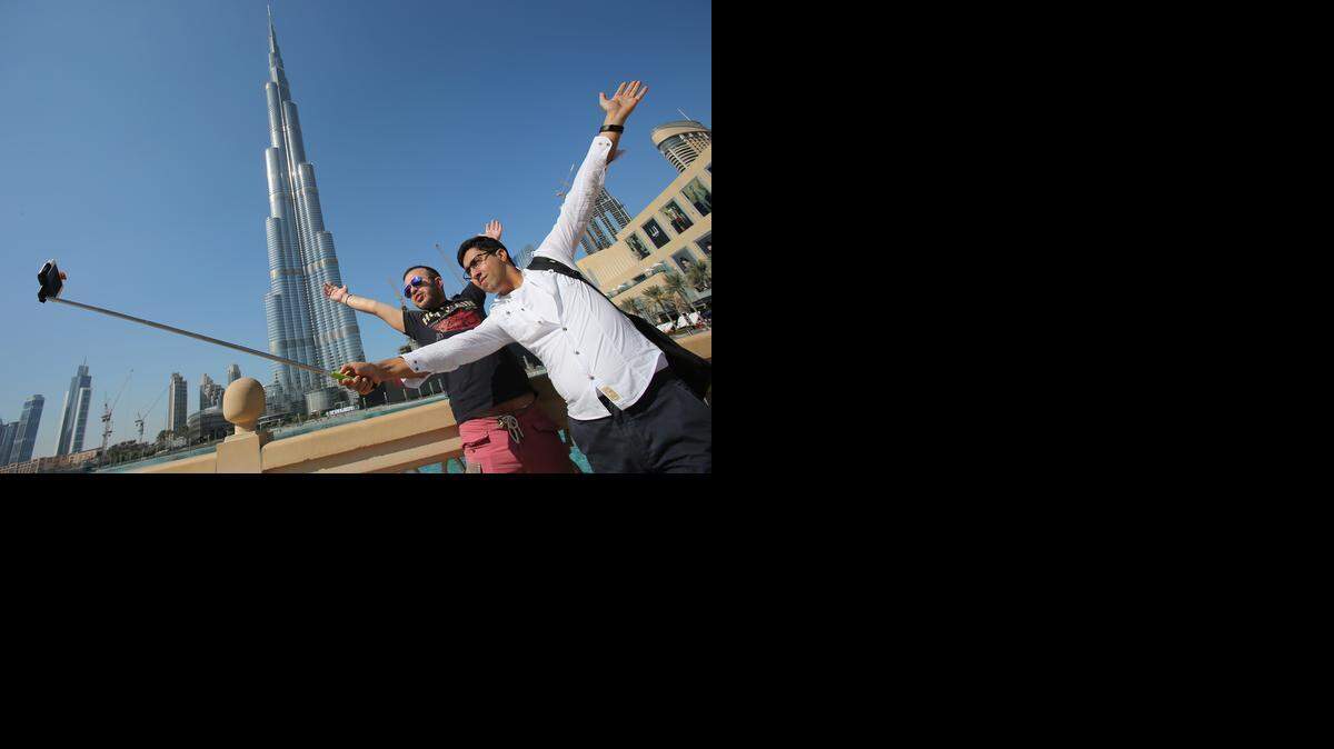 
In this Tuesday, Jan. 6, 2015 photo, Rasul Alekberov holds a selfie stick next to his friend Gudrat Aghayev both tourists from Republic of Azerbaijan while they take a selfie in front of "Burj Khalifa", world's tallest tower in Dubai, United Arab Emirates. Selfie sticks have become popular among tourists because you don’t have to ask strangers to take your picture, and you can capture a wide view in a selfie without showing your arm. (AP Photo/Kamran Jebreili) 

