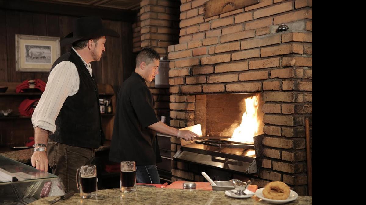 
Kix Brooks watches as Cattlemen’s Omar Valles stokes the Kingsford charcoal fire.

