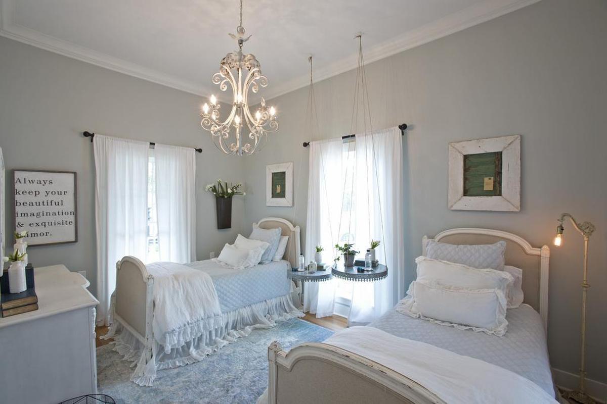 A second bedroom on the ground floor has two single beds and features enlarged windows, white sheer window treatments and suspended bedside tables.