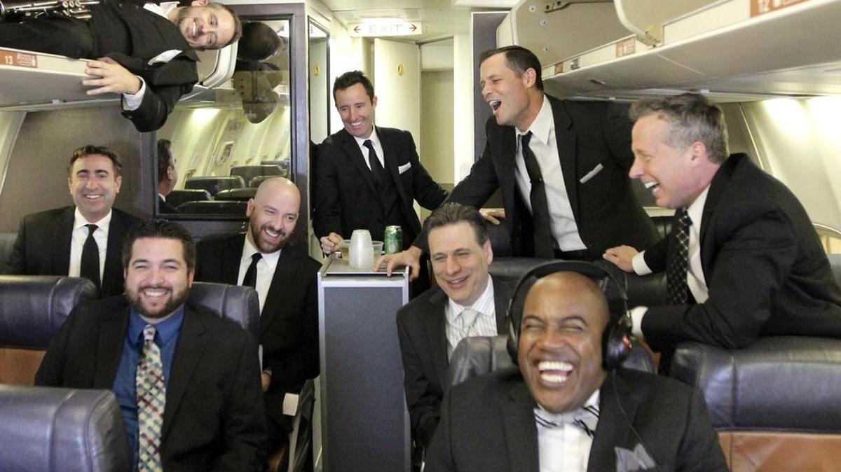 The full Four Day Weekend, from left: Ray Sharp (in luggage rack), Troy Grant, Anthony Bowling, Andrew Hamer, David Ahearn (at beverage cart), Frank Ford, Josh Roberts (standing), Oliver Tull (with headphones) and David Wilk. Grant, Ahearn, Ford and Wilk co-founded the troupe in 1997.