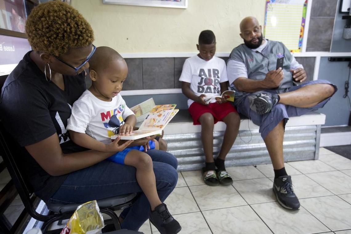 Danielle Davis reads to her nephew Dylan Daniels, 2, as he waits to have his hair cut at Millennium Cuts Barber Studio in August. At right, Terick Jackson reads to barber Roger Foggle.
