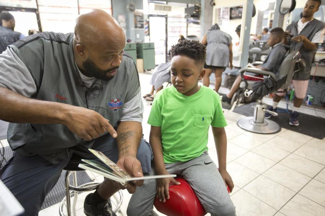Barber Roger Foggle reads with Carter Johnson at Millennium Cuts Barber Studio.