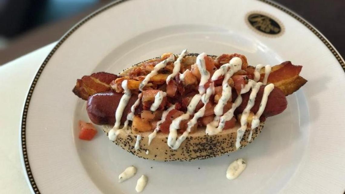 The Hawg Heaven BLT Dawg: East-West Kobe beef frank, crispy thick-cut bacon, Italian-inspired double tomato bruschetta, and a Korean fusion smoky bacon kimchee instead of lettuce, topped off with a French-inspired fine herb aioli sauce and served on a poppy seed bun.