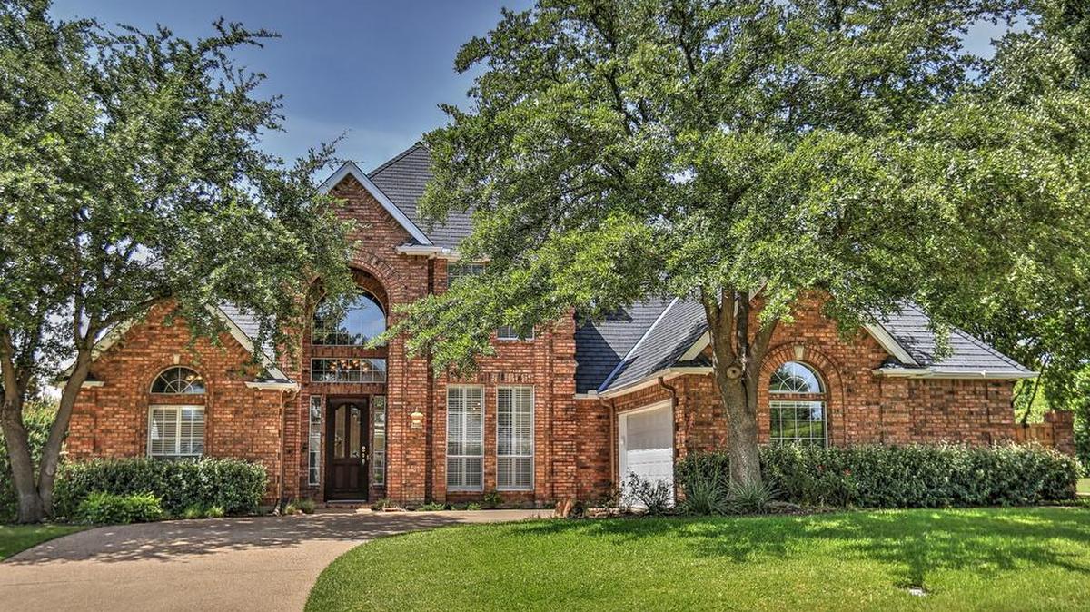 The home is located on a spacious corner lot with a manicured lawn and shady trees.