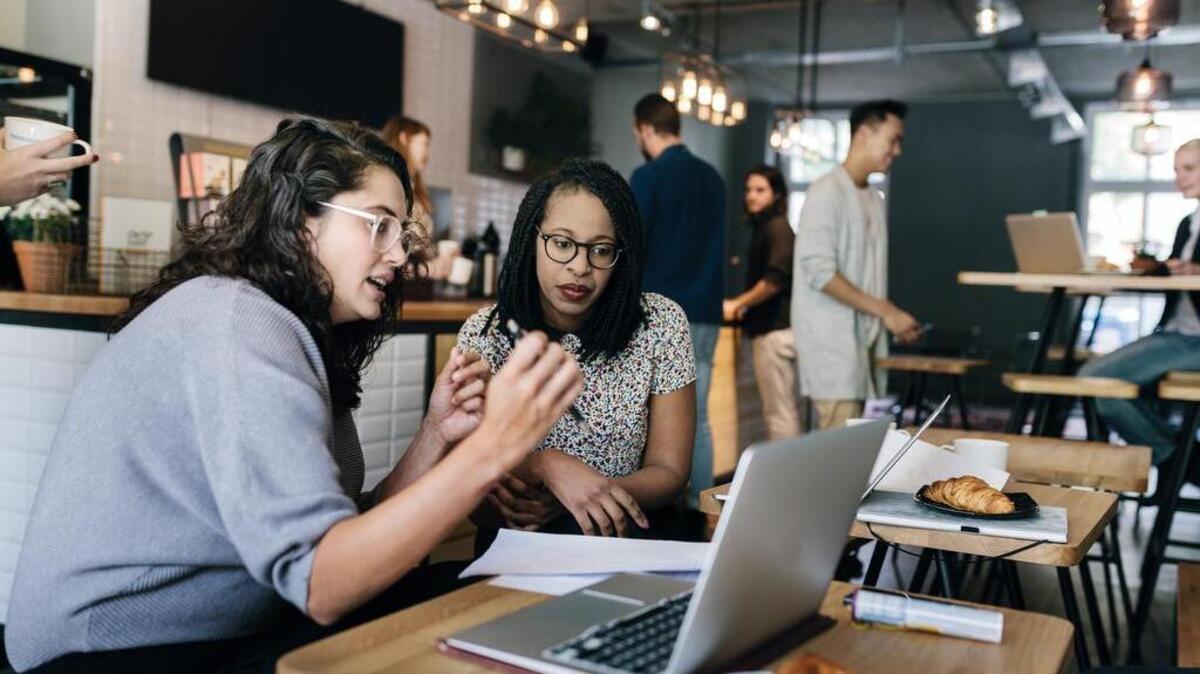 Two young business partners discuss ideas while sitting in a busy cafe.