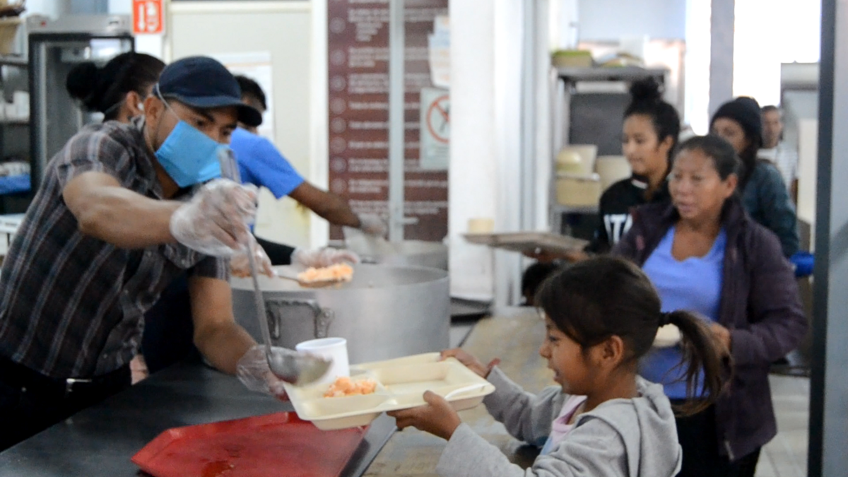 Trabajadores y voluntarios del alberge sirven comida a inmigrantes.