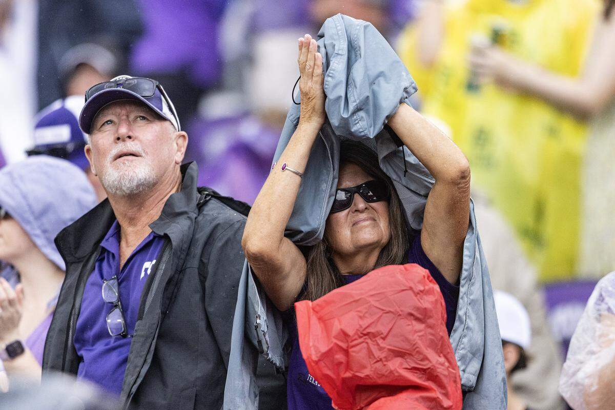 A fan takes cover under her raincoat as it begins to rain in the first half of a Big XII football game between the TCU Horned Frogs and the Baylor Bears at Amon G Carter Stadium in Fort Worth on Saturday, Oct. 18, 2025.
