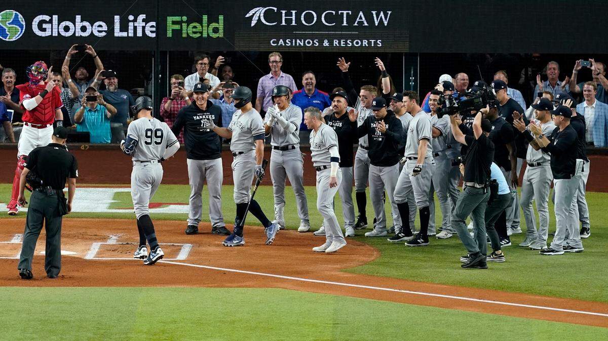 New York Yankees’ Aaron Judge (99) approaches home plate as teammates come out to congratulate him after hitting a solo home run, his 62nd of the season, in the first inning of the second baseball game of a doubleheader against the Texas Rangers in Arlington on Tuesday. With the home run, Judge set the AL record for home runs in a season, passing Roger Maris. Umpire Randy Rosenberg and Rangers catcher Sam Huff also stand by watching the play. (AP Photo/Tony Gutierrez)