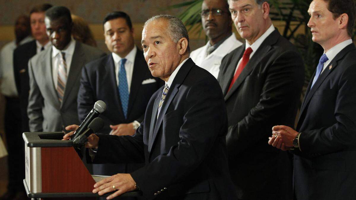 A man stands at a podium, with other men in the background.