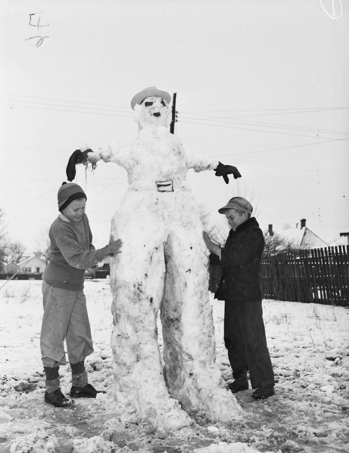 March 1, 1942: “J.V. Perdue Jr. and Gerald Perdue making a snowman. Two children building a tall snowman that has separate legs, instead of a large snowball as the base. The snowman has hat, gloves and belt buckle made from twigs.”