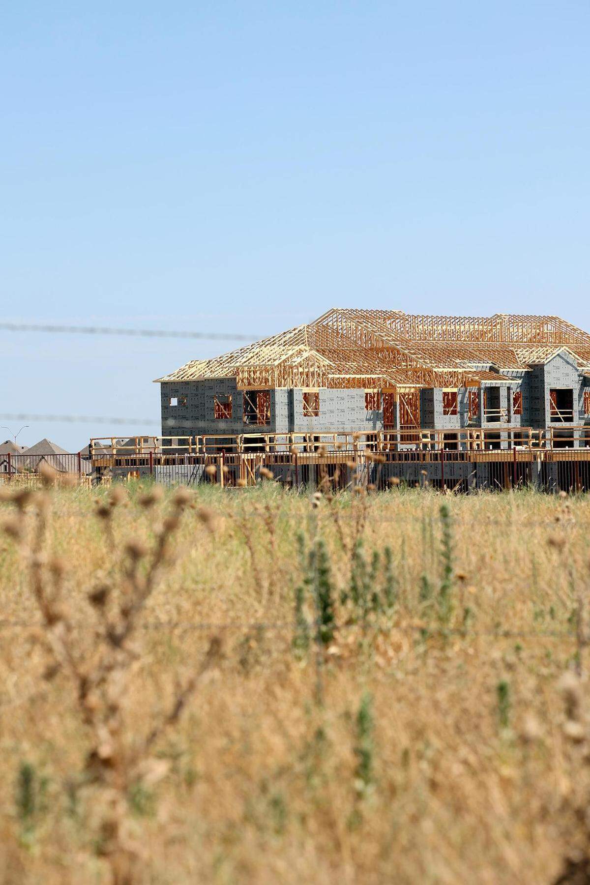 A housing development under construction in the distance with a dry grass field in the foreground.