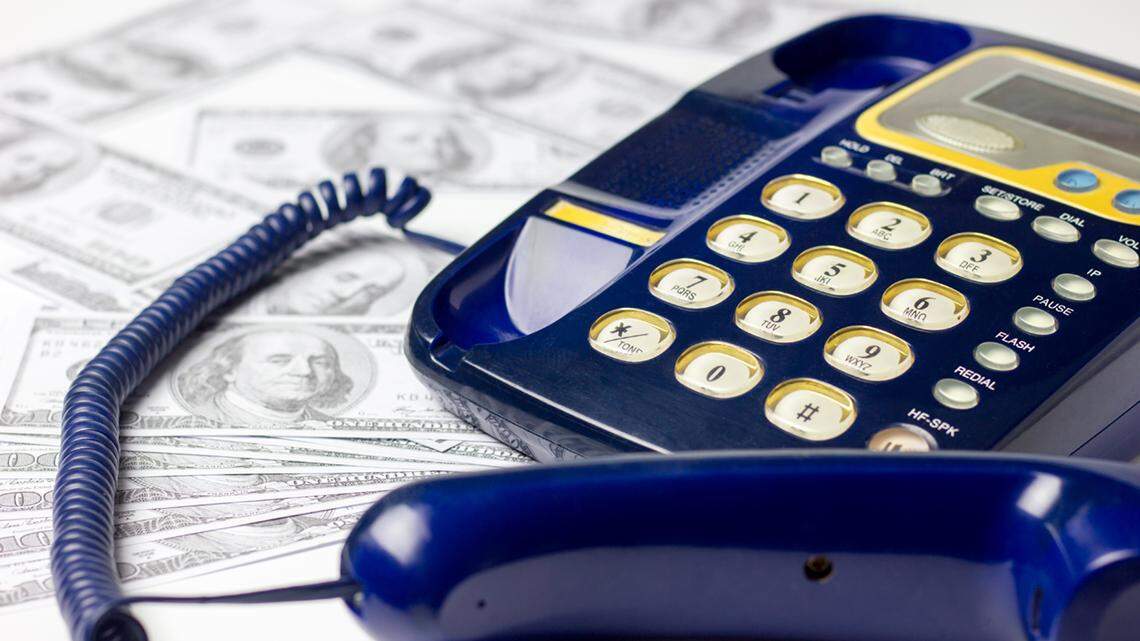 Many American United States 100 dollar bills scattered beside a landline phone on a white background. 