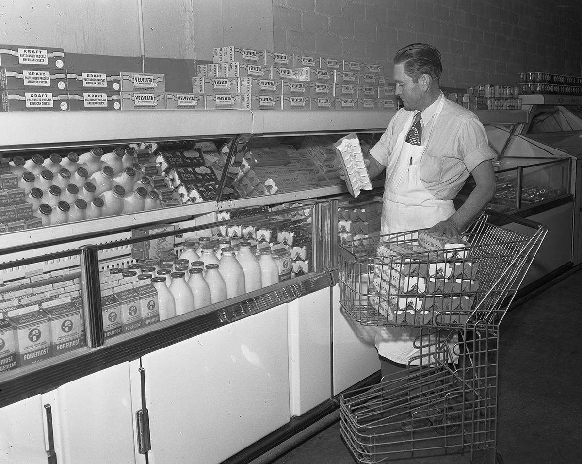 Oct. 15, 1952: Partial interior view of A.L. Davis Food Store No. 3., 2800 Azle, Texas. Shown is L.A. Duke, manager, stocking milk and egg supplies.