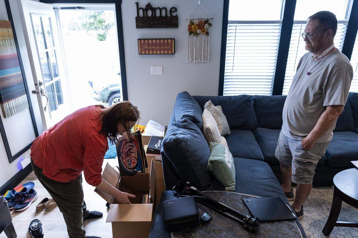 Amy bends down to look through records in a brown cardboard box while Kevin watches to her right.