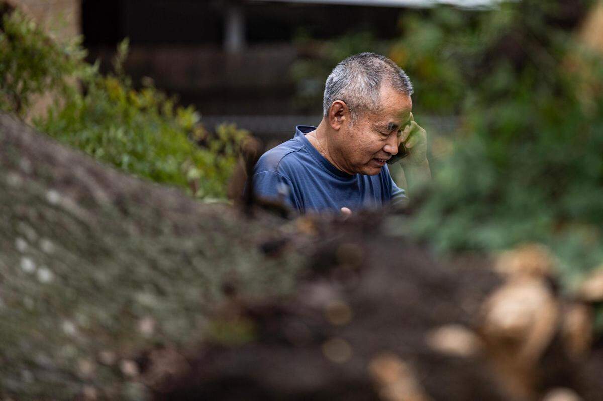 Xinghe Qu, a 25-year Fort Worth resident, talks with a roofing company on the phone after a large tree fell on to his roof due to strong winds in a heavy thunderstorm the night before on the 3500 block of Valencia Court in Fort Worth on Thursday, Oct. 5, 2023.