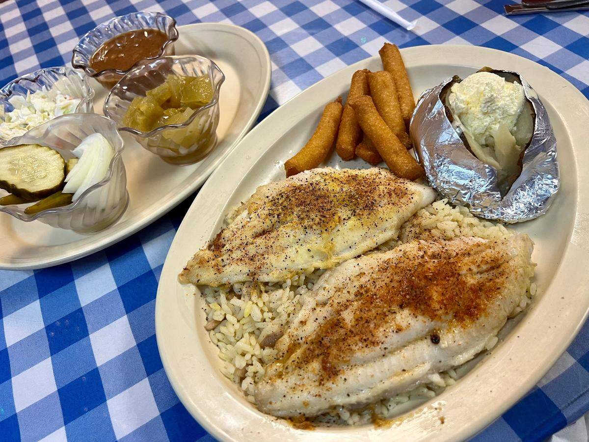 Broiled catfish with hush puppies, baked potato, green tomato relish, pintos and pickles at Catfish Sam’s in Arlington, Texas, March 21, 2023.