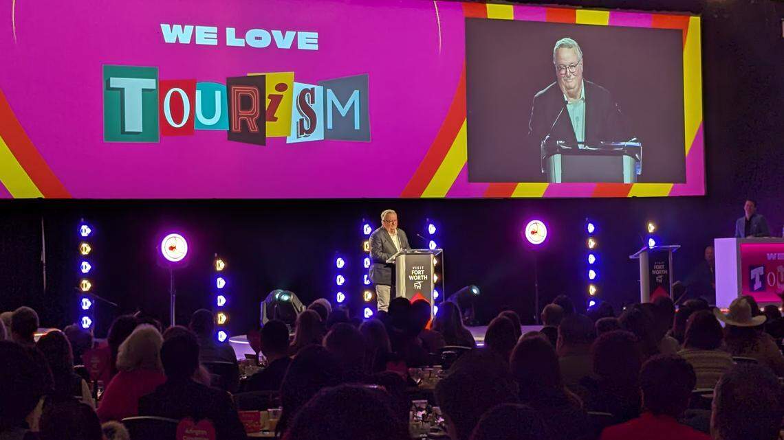 A guy standing on a stage with the word "we love tourism" behind him. 