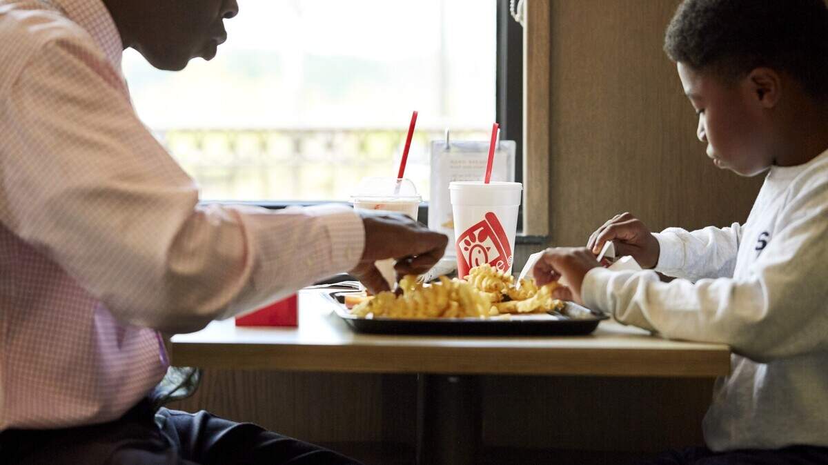 A man and young boy sit across from each other inside a Chick-fil-A restaurant with a tray of fries between them.