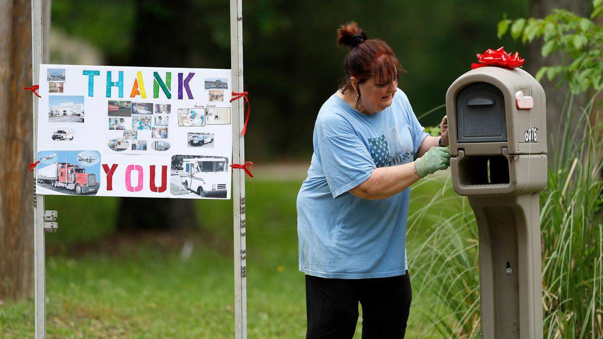 Carol Salers examines her mailbox next to a sign she put up on her yard thanking the various professions of service providers who are working during the new coronavirus pandemic, Saturday, April 4, 2020, in Brandon, Miss. Salers said she wanted to honor everyone from medical professionals to delivery personnel and grocery store employees for their services. (AP Photo/Julio Cortez)