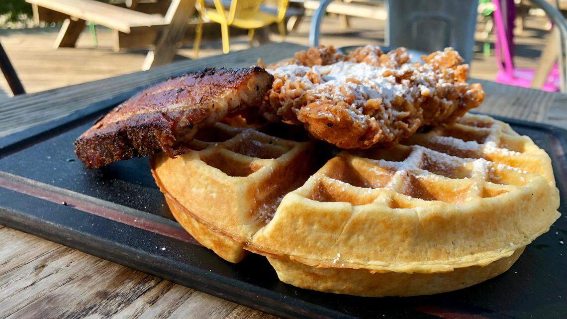 Chicken-and-waffles with a side of bacon on the Woodshed Smokehouse breakfast menu.