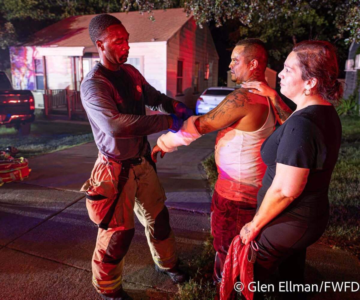 A firefighter treats Leon Segura, who had cuts and burns after he punched through a glass door and went into a burning home to rescue two children in Fort Worth on Thursday, June 25, 2026.