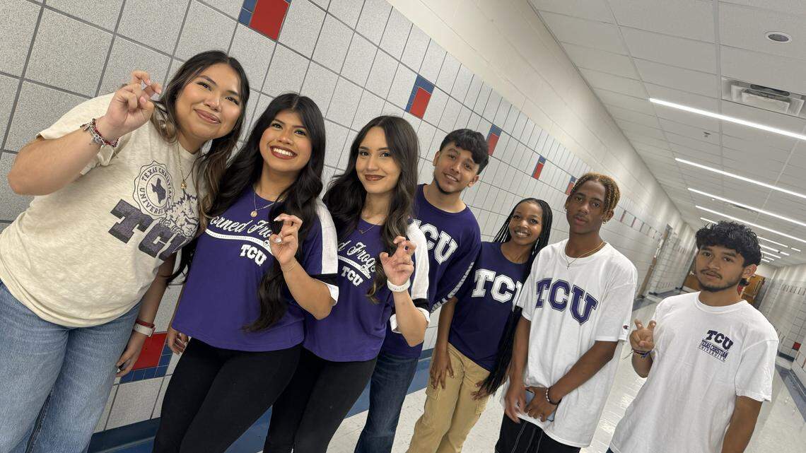 A line of seven high school students in TCU shirts posing in a high school hallway. Most are holding up their index and middle fingers, crooked in the fashion of TCU’s frog sign.