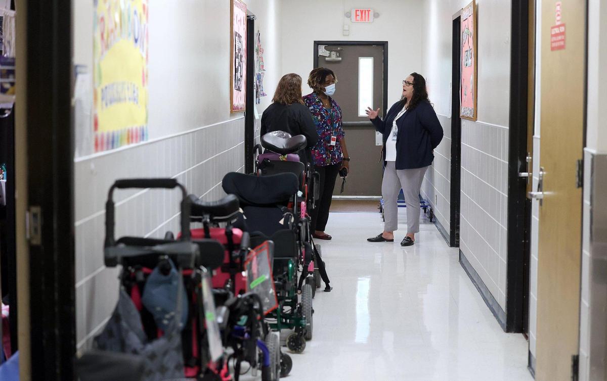 Superintendent Ramsy stands at the end of a hallway lined with wheel chairs on the left side at Jo Kelly School, a school for medically fragile children. She is talking to two other school officials. 
