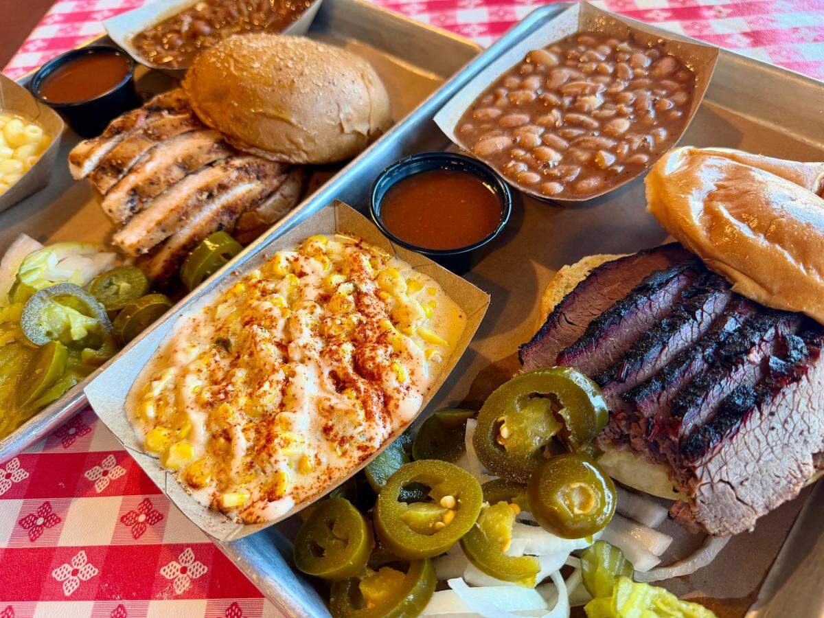 For less than $20 on Monday nights, the Cousin’s BBQ locations on McCart Avenue in south Fort Worth, Texas, and in Crowley, Texas, sell two-for-one sandwiches and sides. Shown: sliced brisket and sliced boneless chicken sandwiches, with elote (center) and “Bootsie’s cowboy beans,” seen july 21, 2025.