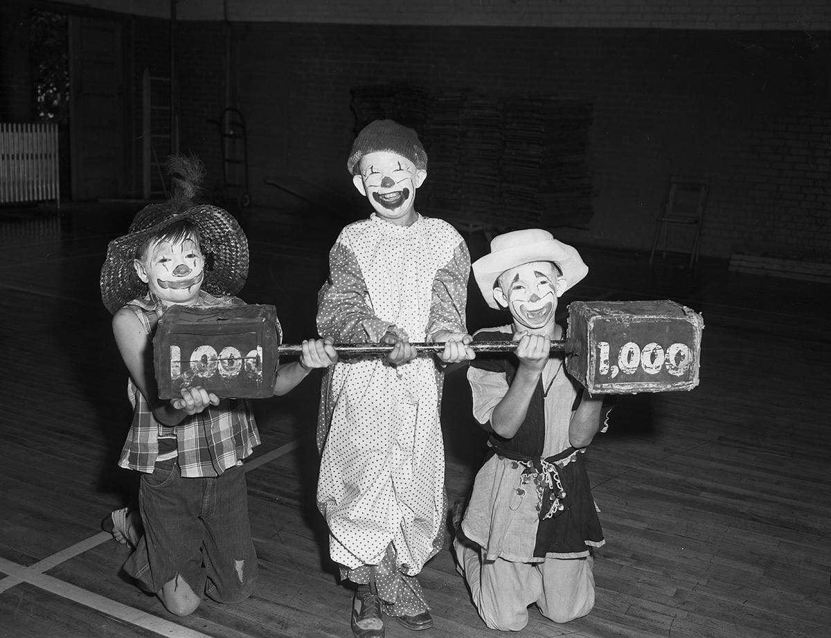  The three children dressed as clowns are holding a fake dumbbell labeled as 1,000 pounds.