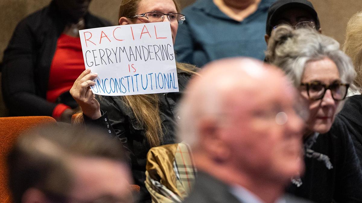 Meeting attendee Crystal Betts holds up a sign protesting the proposed redistricting of the county during a Commissioners Court Meeting at the Tarrant County Administration Building in Fort Worth on Tuesday, May 6, 2025.