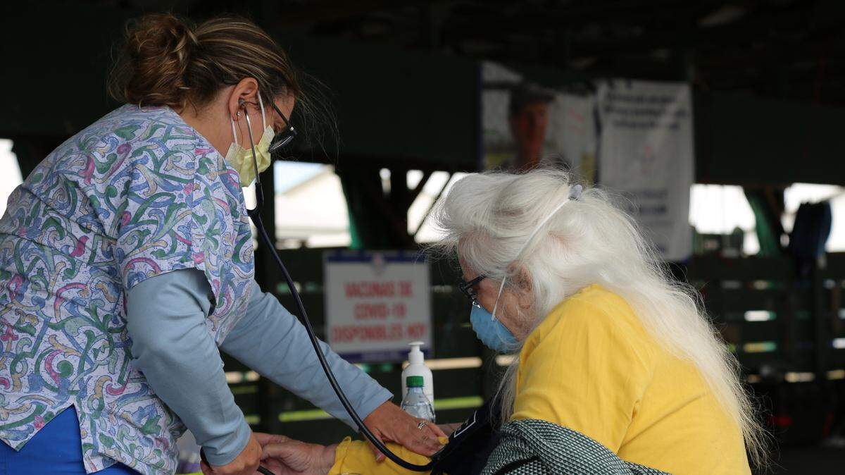 A woman in scrubs takes the heart rate and blood pressure of a second woman.