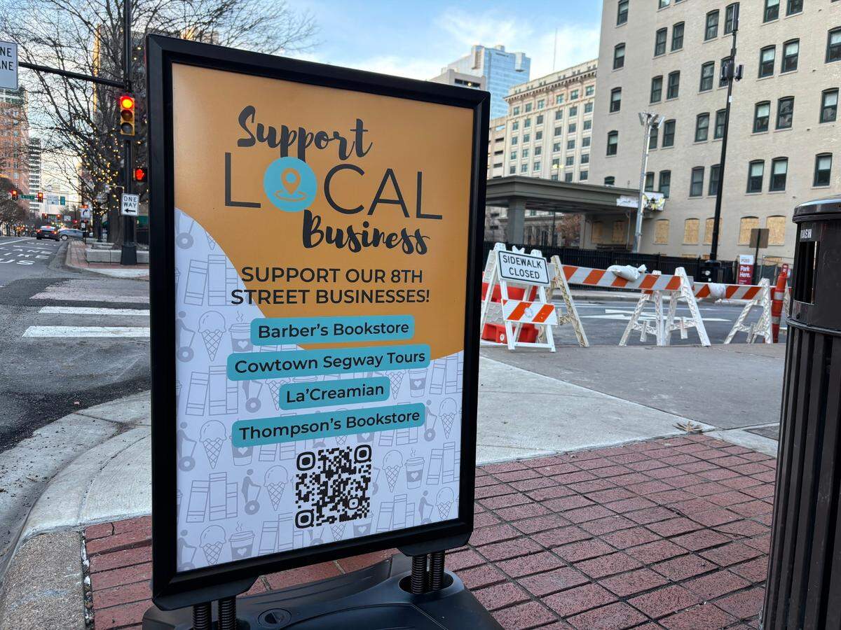 A promotional sign invites passersby to learn more about and patronize struggling businesses on West 8th Street near the site of the explosion that rocked the Sandman Signature Hotel earlier this month.