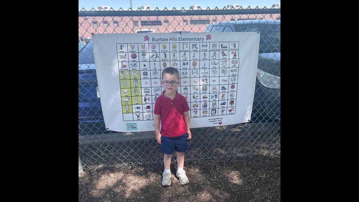 4-year-old Elliott stands in front of a Burton Hill Elementary playground communication board.