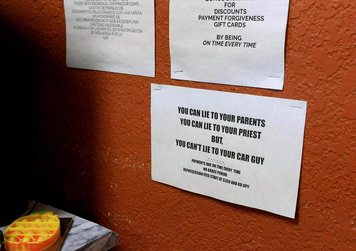 Paper signs informing customers of policies hang from Wayne Harrison’s office wall at Owl Own It Auto Sales on Tuesday, April 19, 2022, in Fort Worth.