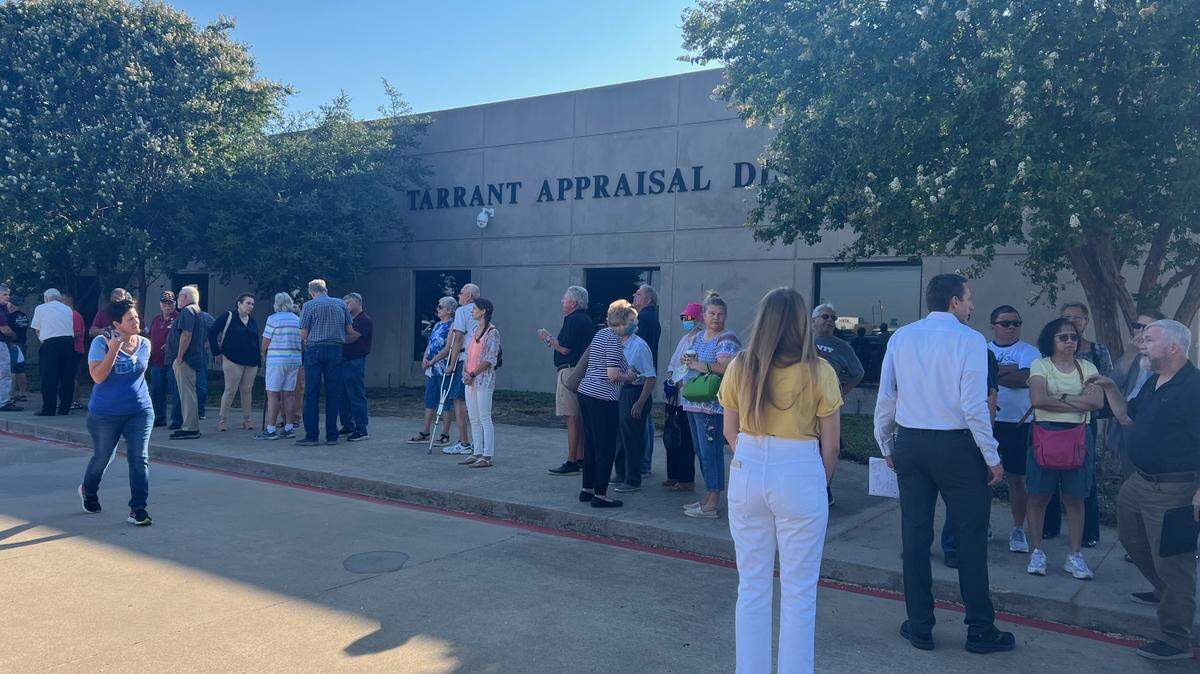 A crowd of people stand along a sidewalk and parking lot outside a building where the Tarrant Appraisal District Board met Thursday.