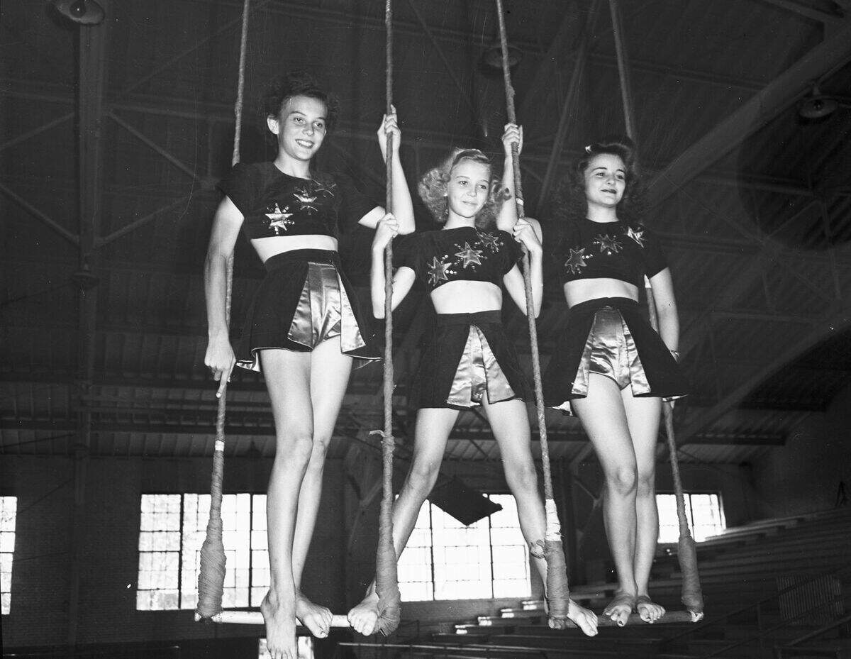 The Starettes are wearing matching costumes consisting of a blouse with three stars and a skirt. They are standing on swings handing from the ceiling.