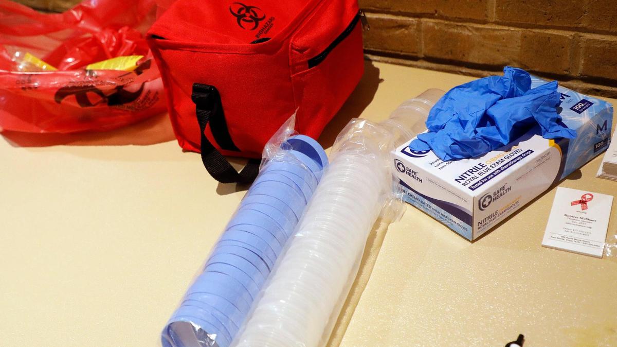 Many different items are scattered on a table, including rolls of plastic items, a red bio hazard soft cooler and rubber gloves.