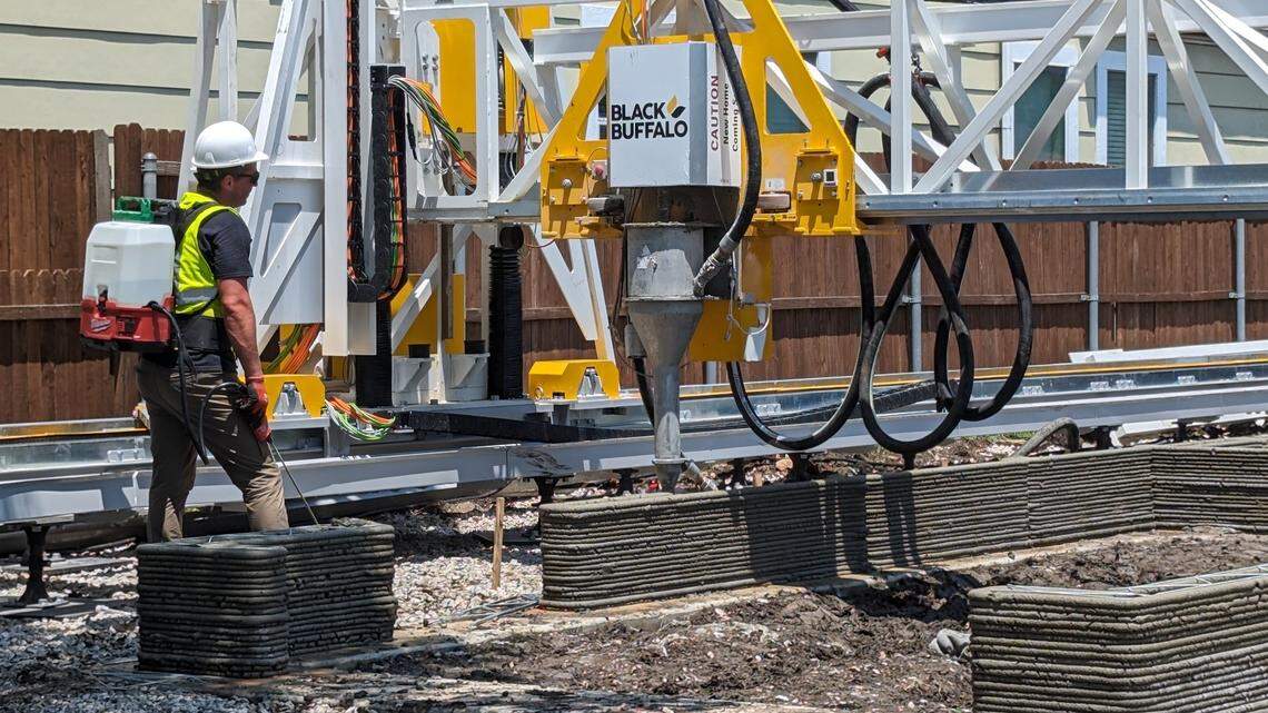A construction worker stands in front of a robot dispensing concrete.