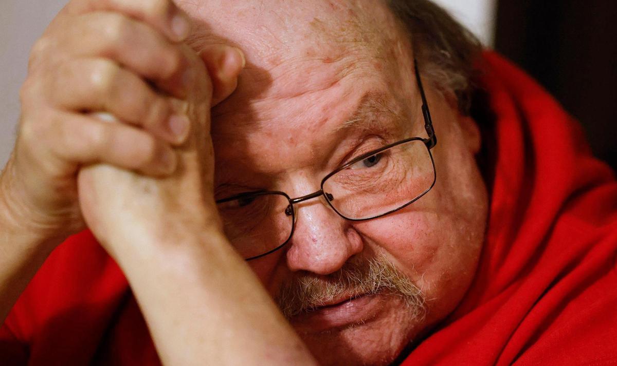 A tight shot of the face of a man wearing glasses with his hands clasped together in front of his face.