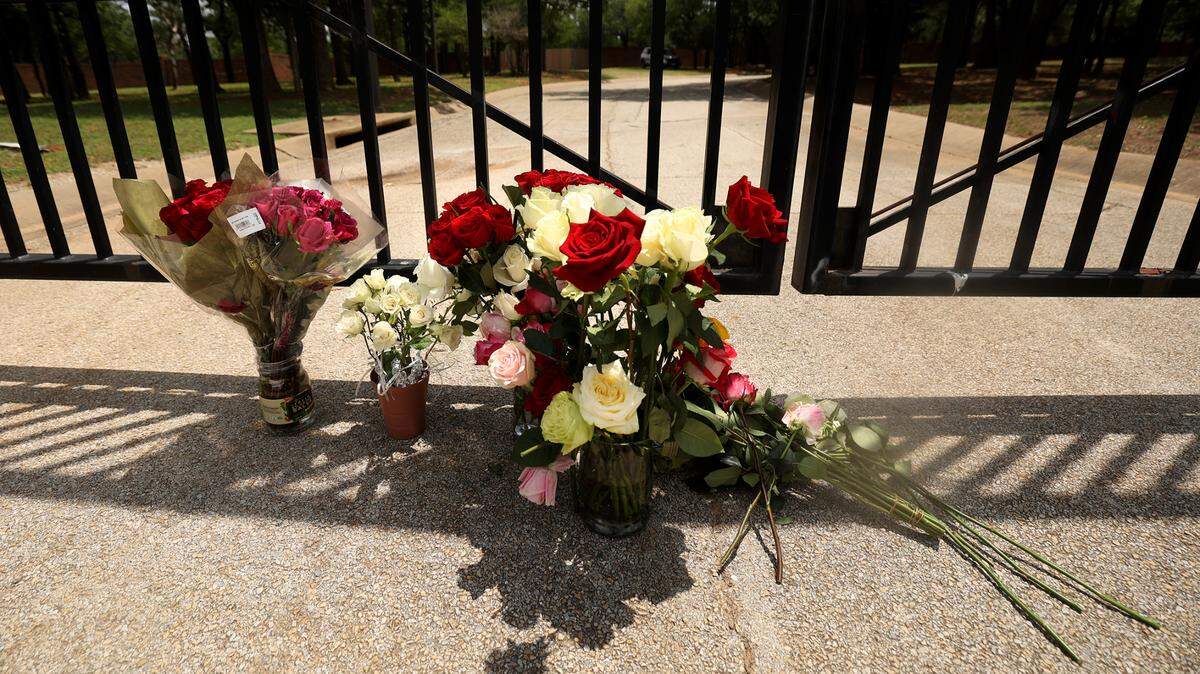 Numerous bundles of roses, red and white, sit on a concrete driveway that leads to a black iron gate.