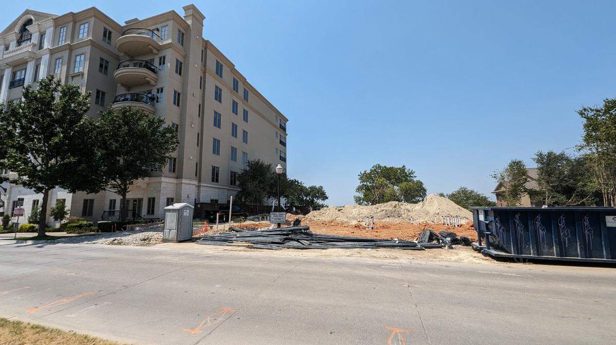 An empty lot with construction equipment next to a condo building. 