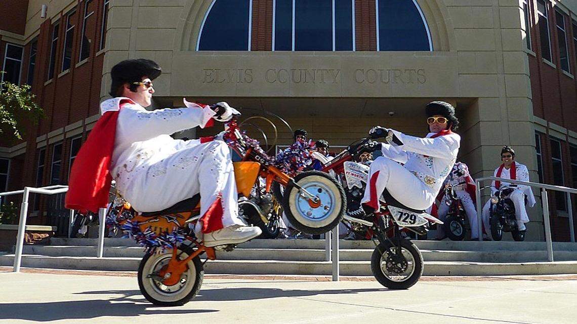 A couple members of “The World Famous Wheelie-ing Elvi” pop a wheelie.