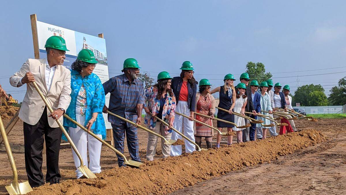 A bunch of smartly dressed people in hardhats doing performative manual labor at a ground breaking ceremony.