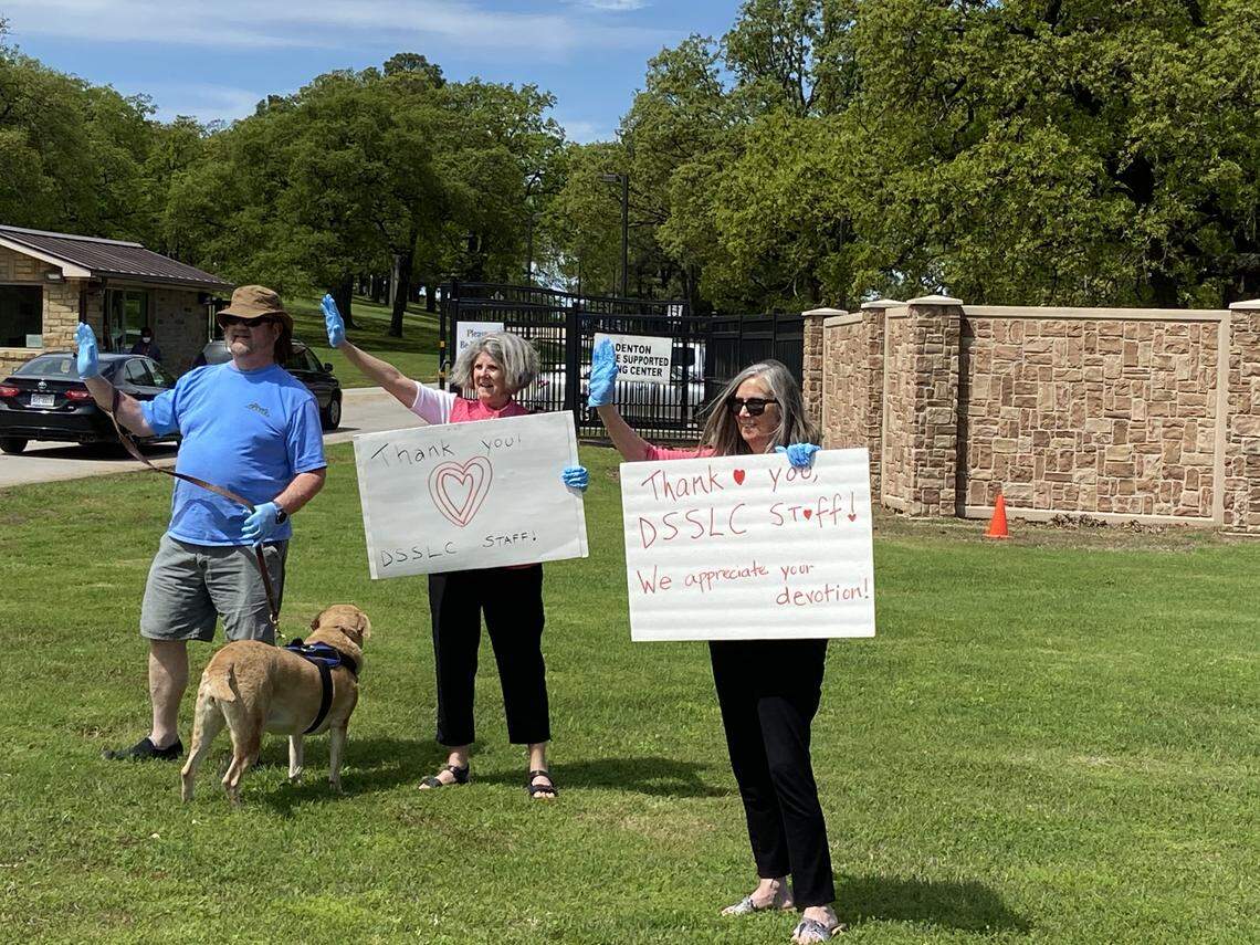 (From left to right) Mike Danks, Sue Monroe and Jenny Ellis stand outside of the Denton State Supported Living Center holding up signs showing support for the staff. Mike and Karen Danks’ 31-year-old daughter lives on the campus, which has 45 cases of the coronavirus.