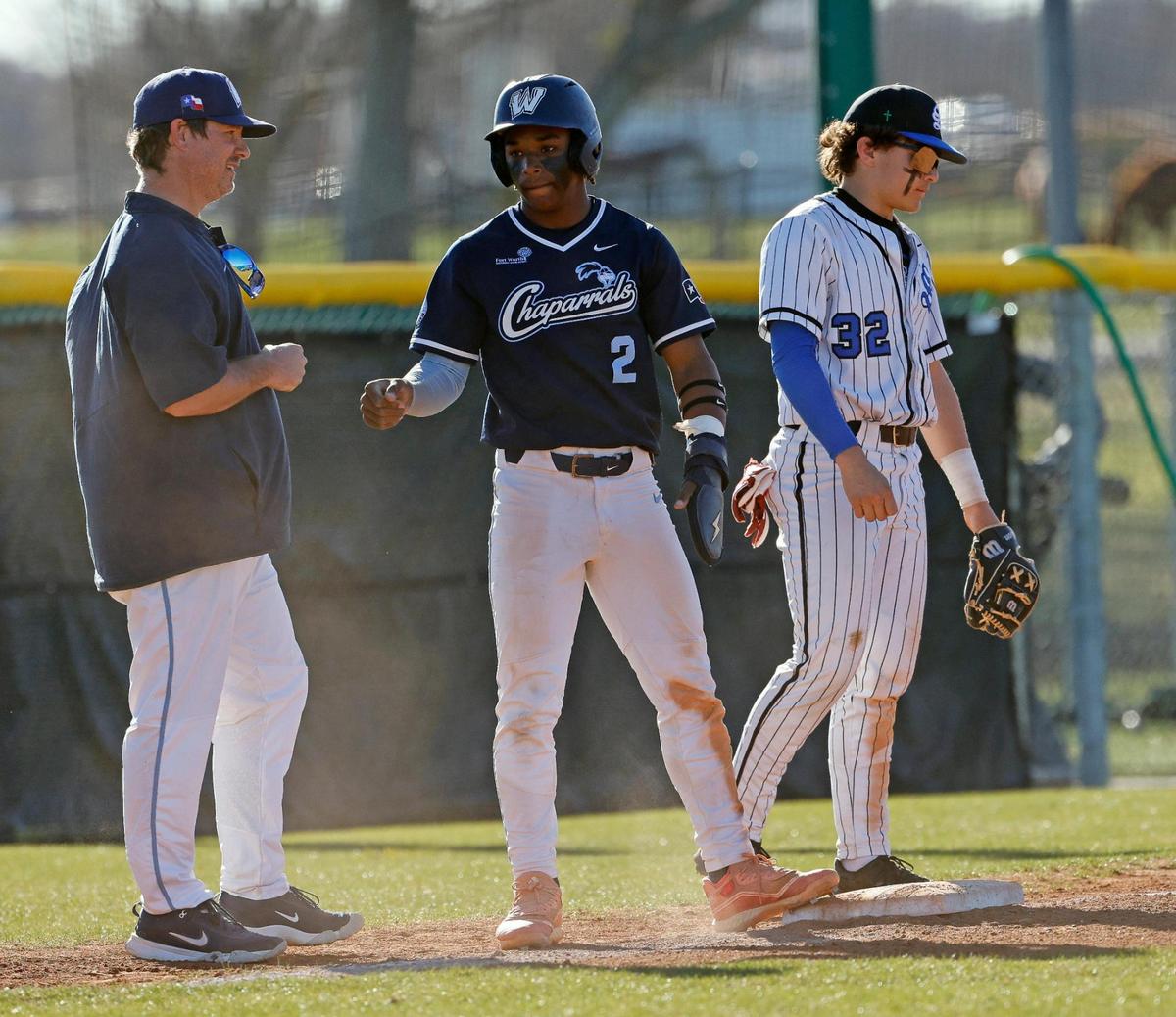 Wyatt catcher Jorvorskie Lane (2) fist bumps third base coach Jason Starnes after reaching third in front of Southwest Christian third baseman Josh Blanco (32) during a UIL baseball game at Benbrook High School in Fort Worth, Texas, Thursday, Feb. 22, 2024.