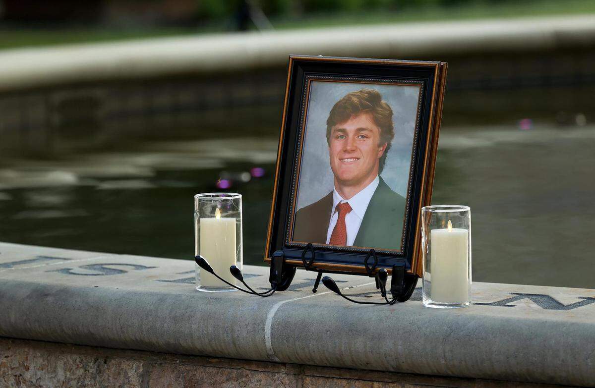 A photo of Wes Smith in a jacket and tie is flanked by white candles on the edge of a calm fountain.