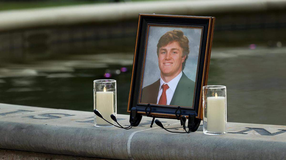 A photo of Wes Smith in a jacket and tie is flanked by white candles on the edge of a calm fountain.