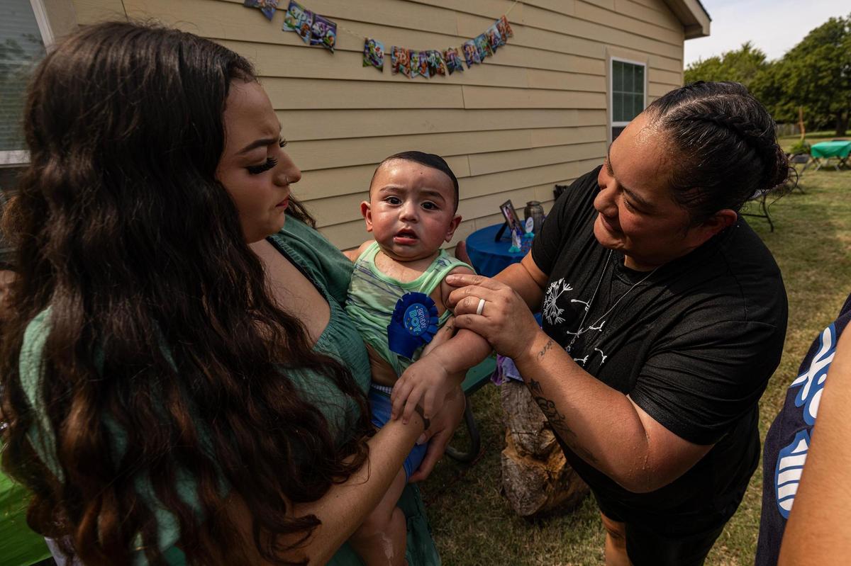 Corina Camacho, left, holds her son Zechariah Emilio, 1, with his grandmother Erica Silva after they slid down the water slide at his birthday party at Camacho’s aunt’s house in Newark on Sept. 14.