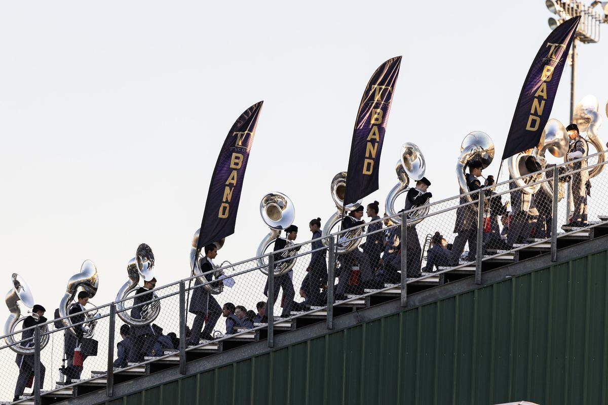 A view of the football stands show tuba players on every level, rising in a diagonal from left to right, as they walk to the top.