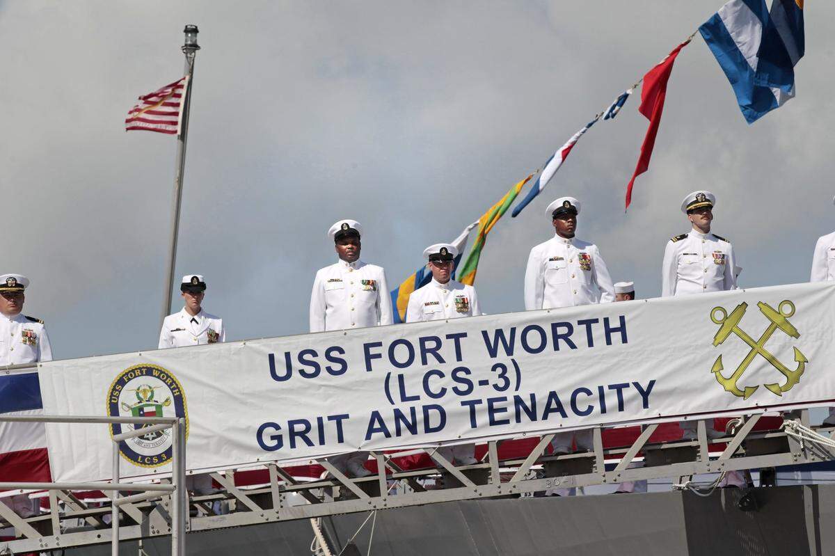 After boarding their ship, crew members stand at attention behind a banner with the ship’s motto, during the commissioning ceremony for the USS Fort Worth in Galveston, Texas, on Sept. 22, 2012.
